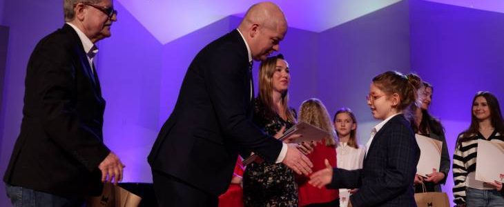 Ubiegłoroczna gala, na scenie w Państwowej Szkole Muzycznej w Płocku prezydent Nowakowski z wiceprezydentem Romanem Siemiątkowskim wręczają nagrodę jednej z laureatek. W tle stoją w szeregu pozostali nagrodzeni.