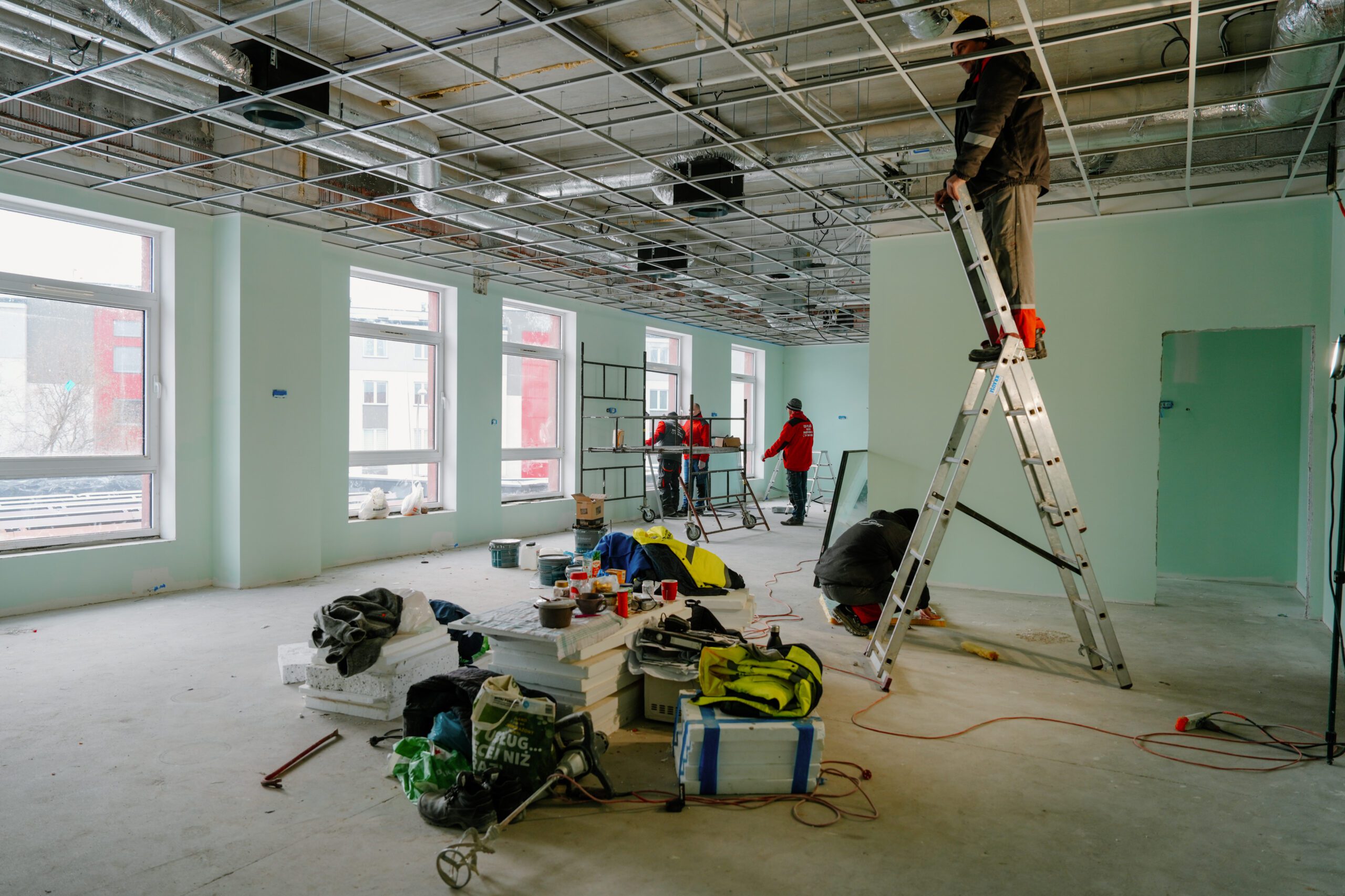 Na pierwszym planie jeden z fachowców na drabinie montuje podwieszany sufit w jednej z sal dla maluchów